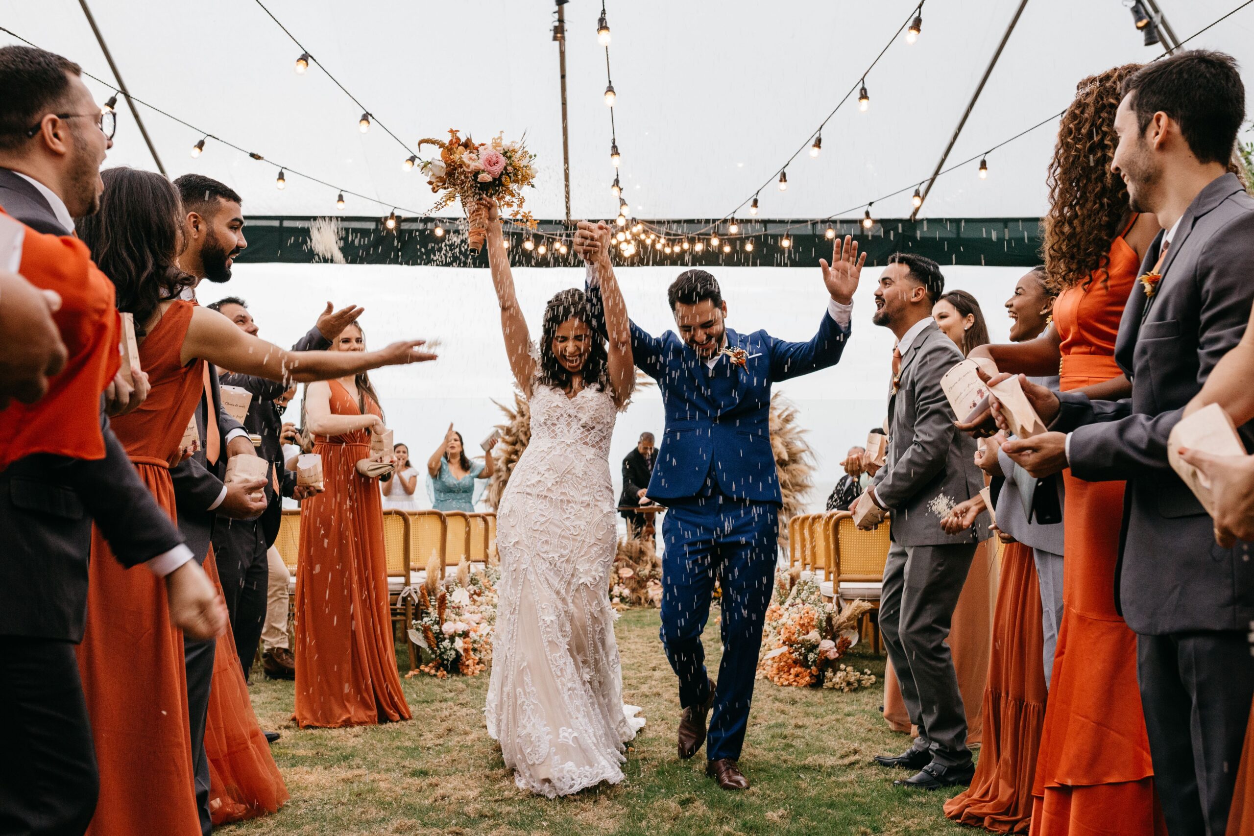 A couple celebrates their wedding with friends outdoors under string lights.