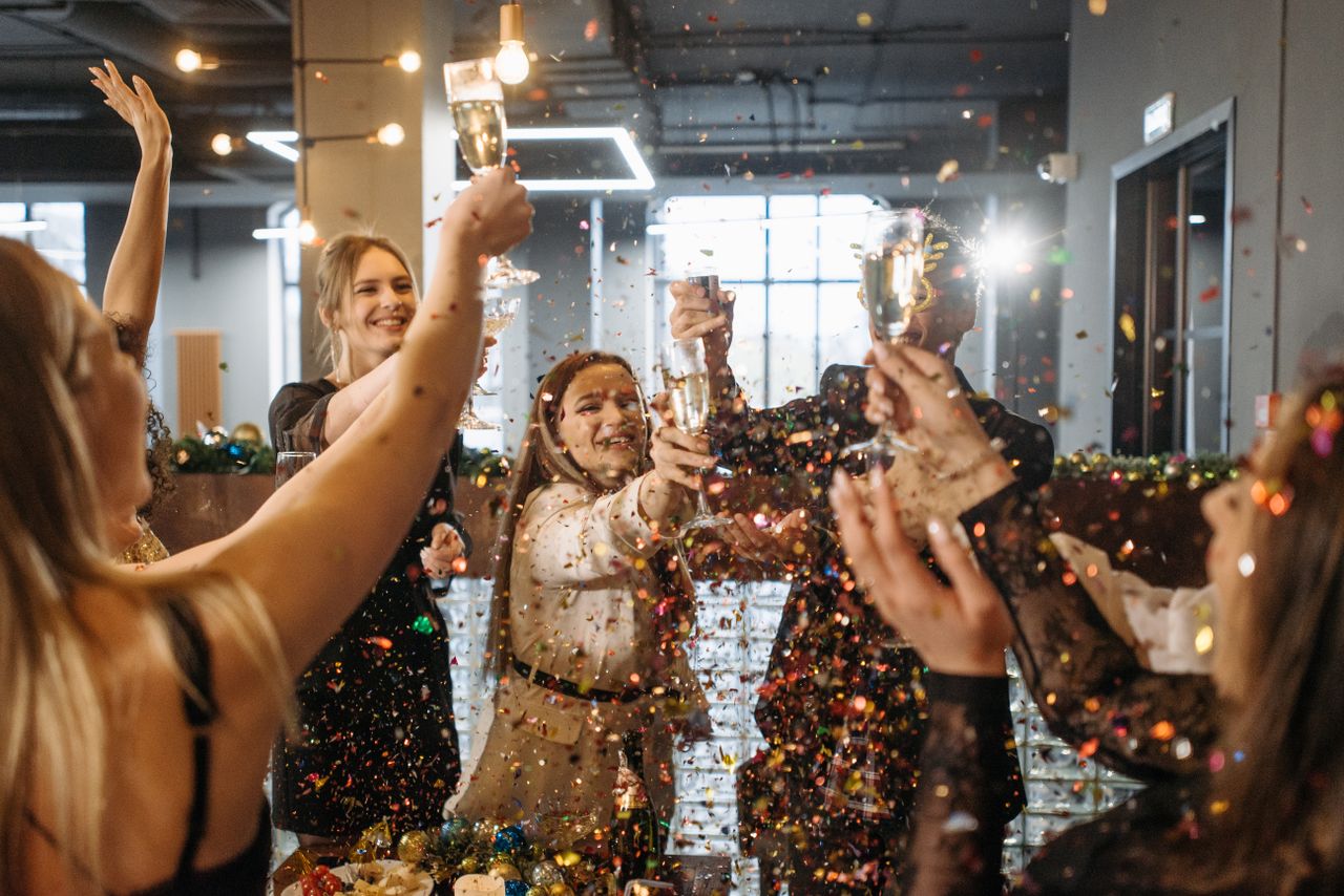 A diverse group of friends celebrating indoors with champagne and confetti.